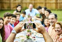 Family gathering in back yard. Taking a picture on their phone. 