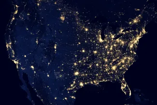 Satellite view of the continental United States at night showing city lights illuminating populated areas across the country.